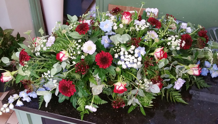 Mixed flower casket spray - cream roses, scabious, blue delphiniums, red chrysanthemum blooms